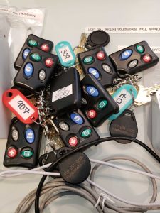 pile of black keyscan garage remote copies along with standard key fob copies and keys